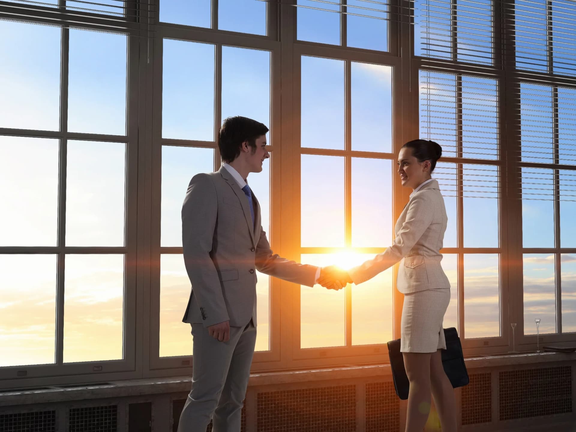 Two business partners shaking hands by an office window